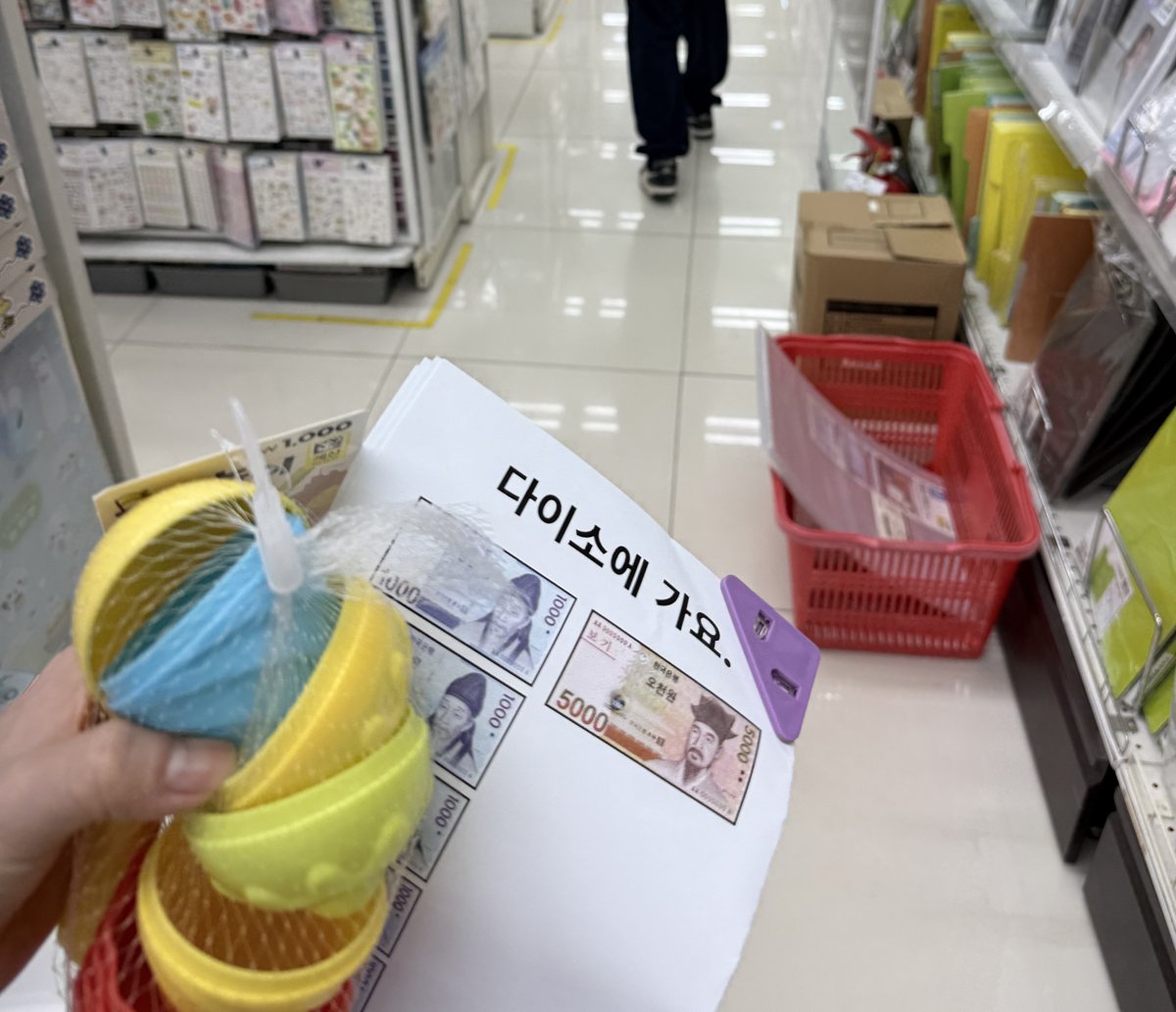 다이소 매장에서 '다이소에 가요' 시각 안내지와 돈 그림을 들고 장보기 연습을 하는 모습
